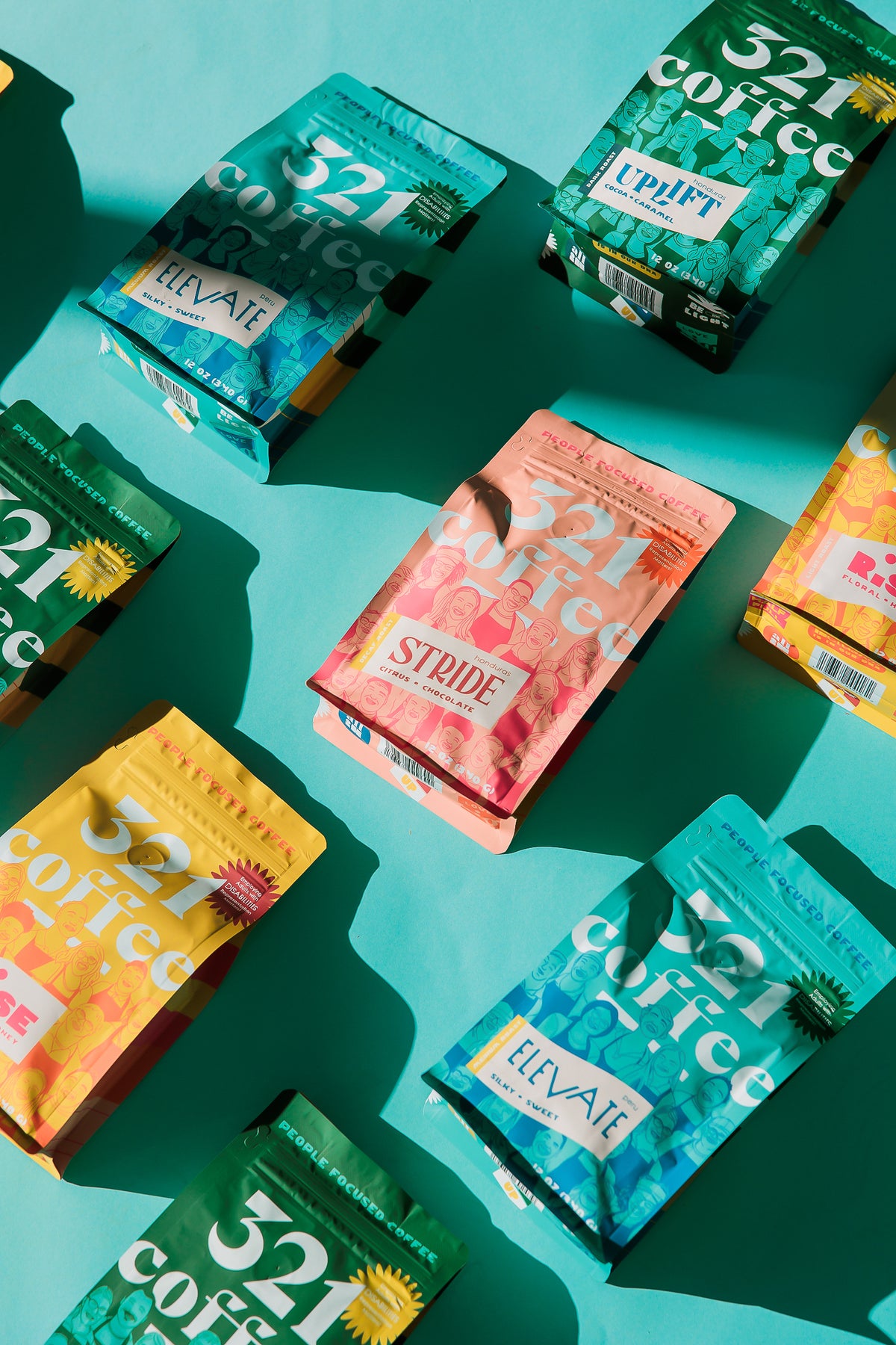 Colorful 12 ounce bags of 321 Coffee are laid out on a teal background. The bags feature a prominent 321 Coffee logo set into a group of sketches of the team.