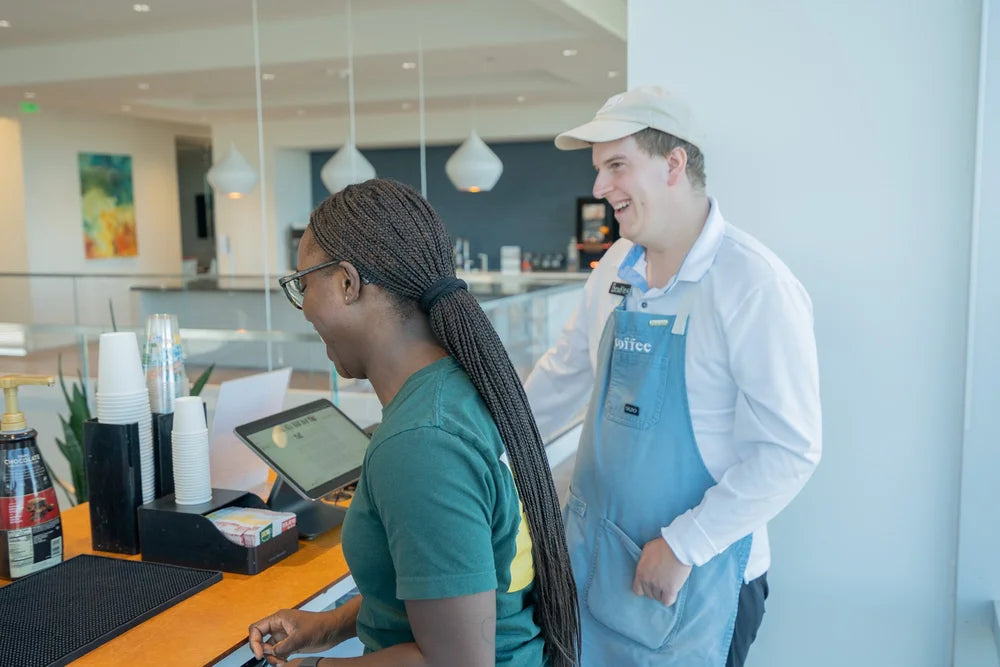 Two members of the 321 Coffee Cart team smile and laugh while serving customers at an office event.