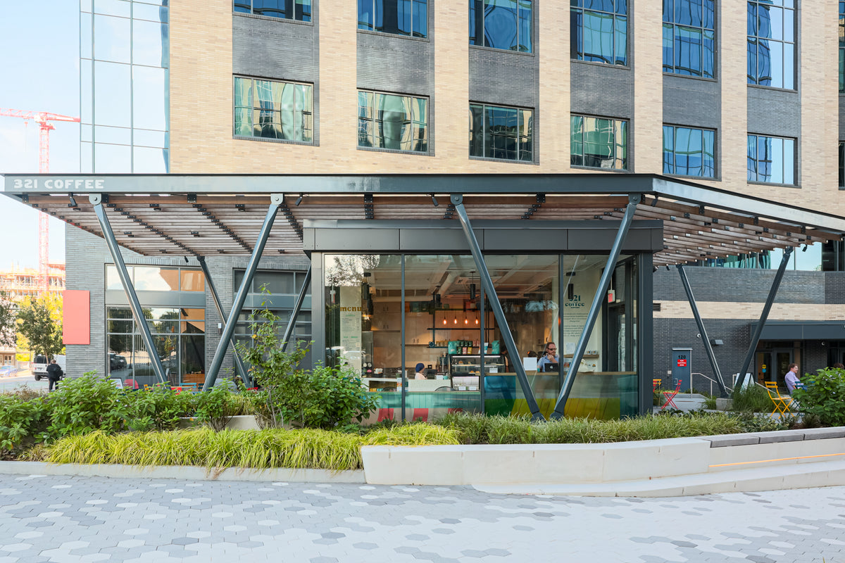 The Downtown Raleigh shop is shown on a sunny spring day. The shop is a unique free standing structure of black metal and large glass walls with an trellis overhangs on both the front and back patios.