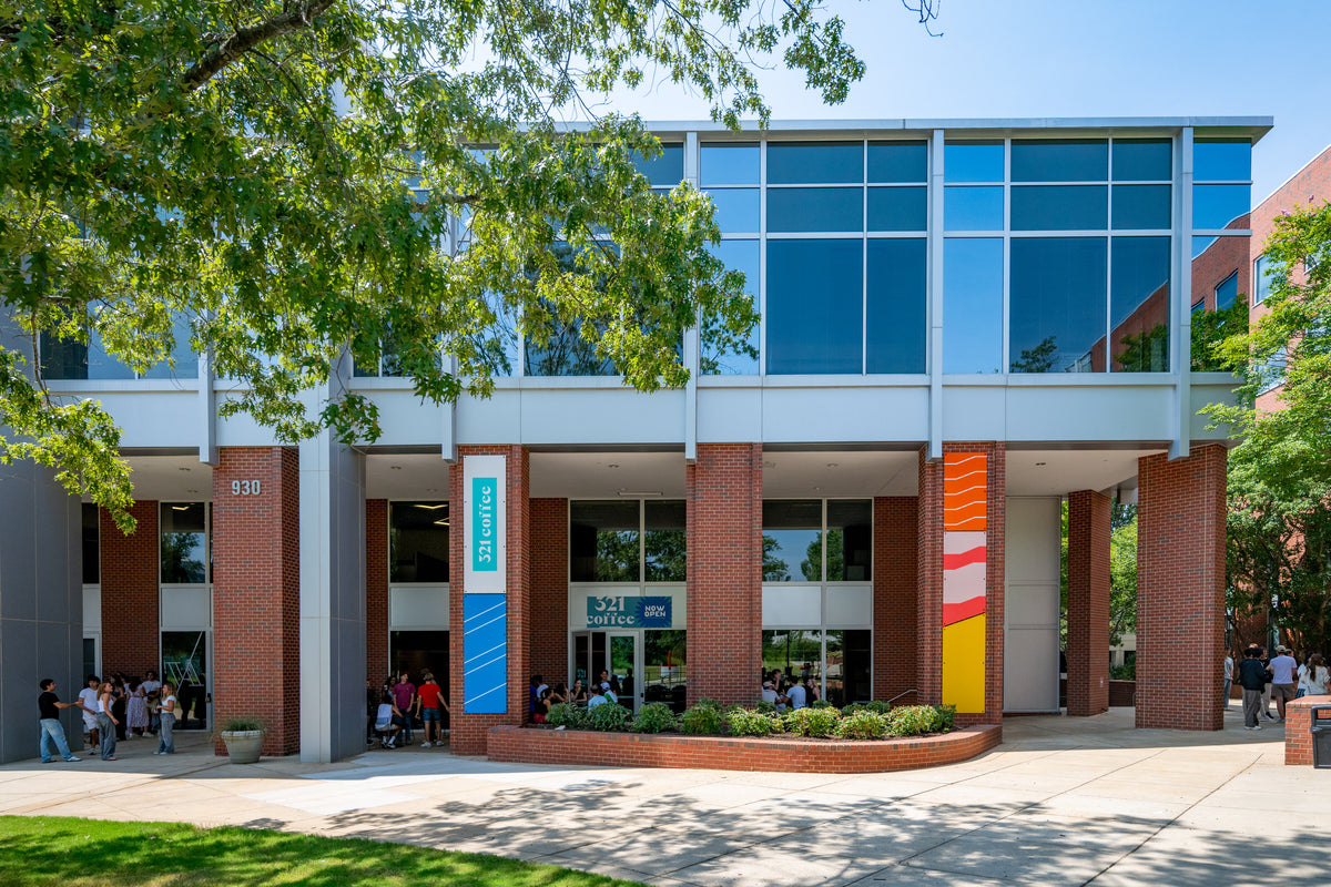 The NC State Centennial shop is in the first floor of a modern two story building with expansive patio space in the front among large brick columns.