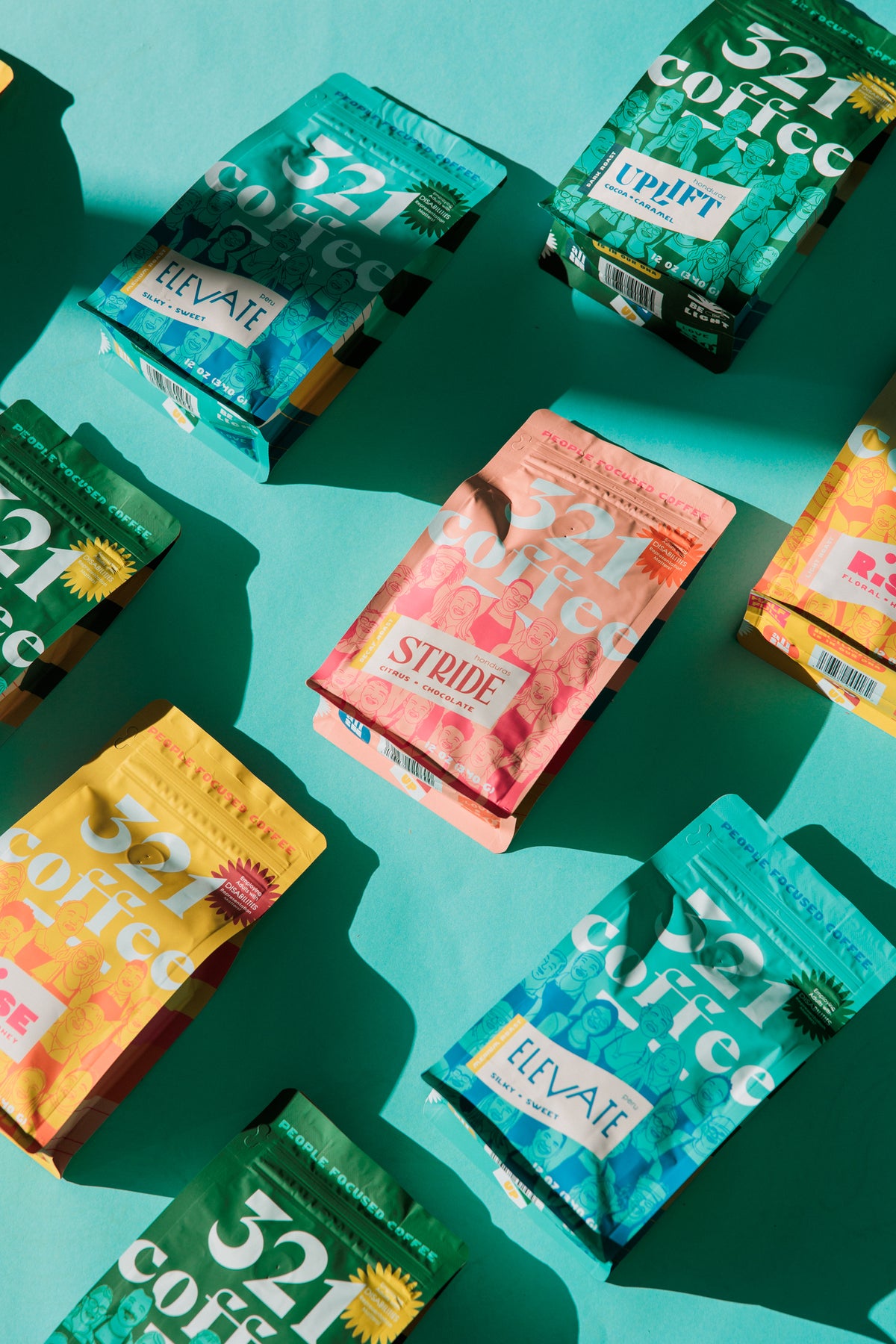 Vibrant teal, green, pink, and yellow bags of 321 Coffee are laid out on a teal background. The packaging features colorful sketches of baristas on the 321 Coffee team.