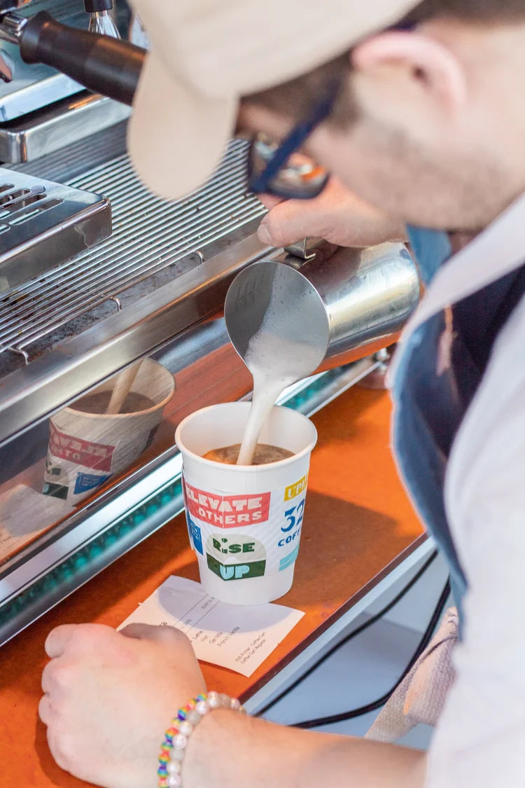 A barista carefully pours steamed milk into a hot latte in front of the espresso machine.