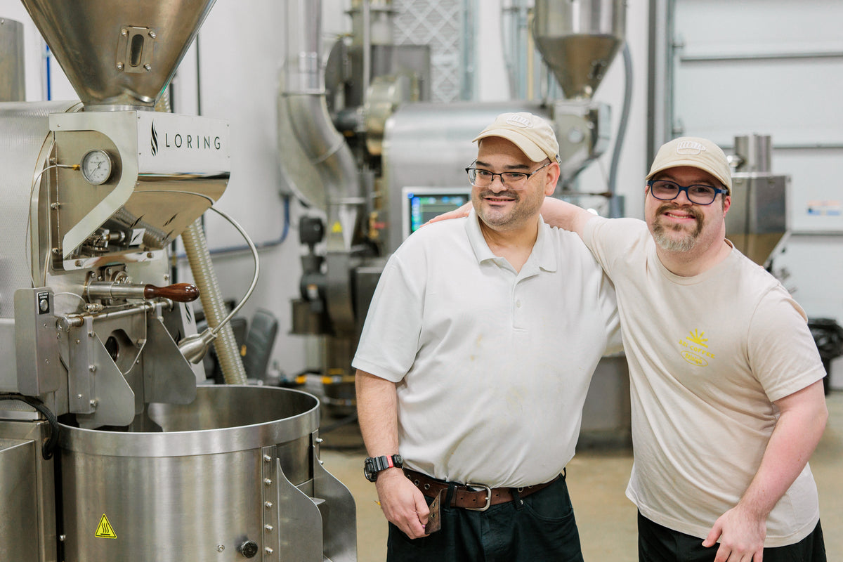 Aaron and Paul, two roasters on the 321 Coffee team stand and smile with their arms around each others shoulders inside the 321 Coffee roastery.