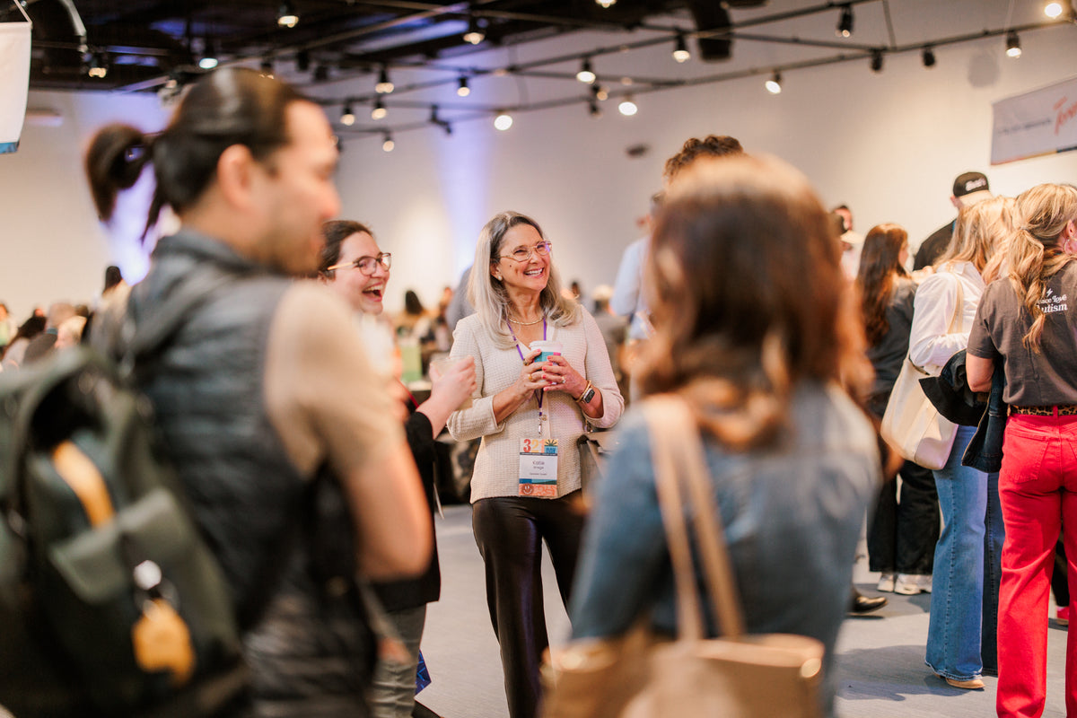 Dozens of people wearing lanyards fill a large room as they stand, talk, and smile while holding cups of 321 Coffee at a catered event.