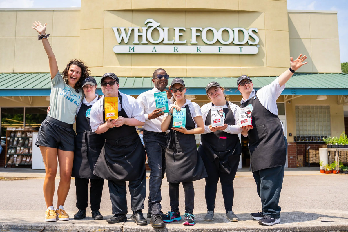 A group of baristas gather for a celebratory photo with co-founder Lindsay in front of a Whole Foods Market with bags of 321 Coffee.