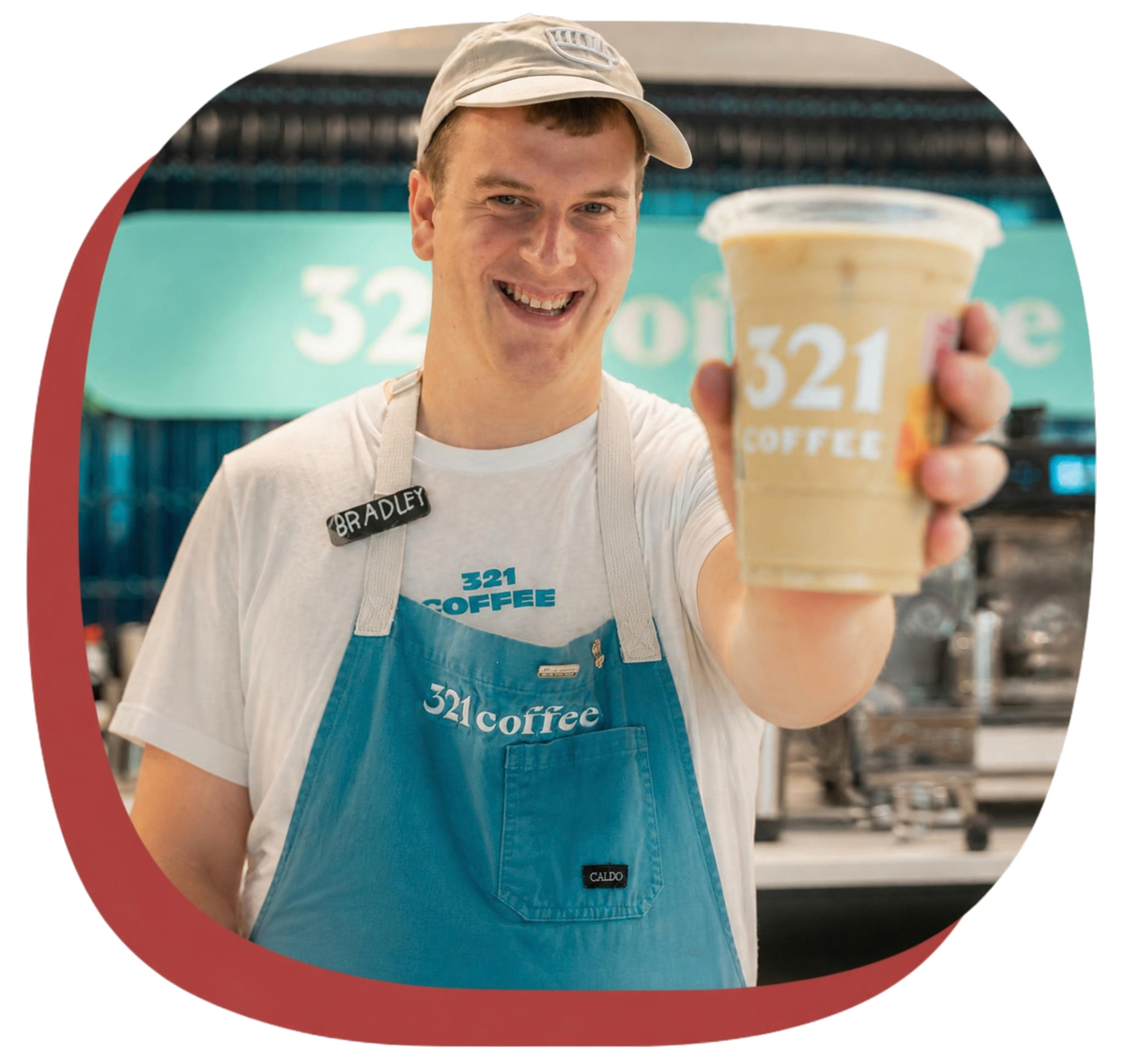 A barista smiles inside a 321 Coffee shop and holds out an iced latte.